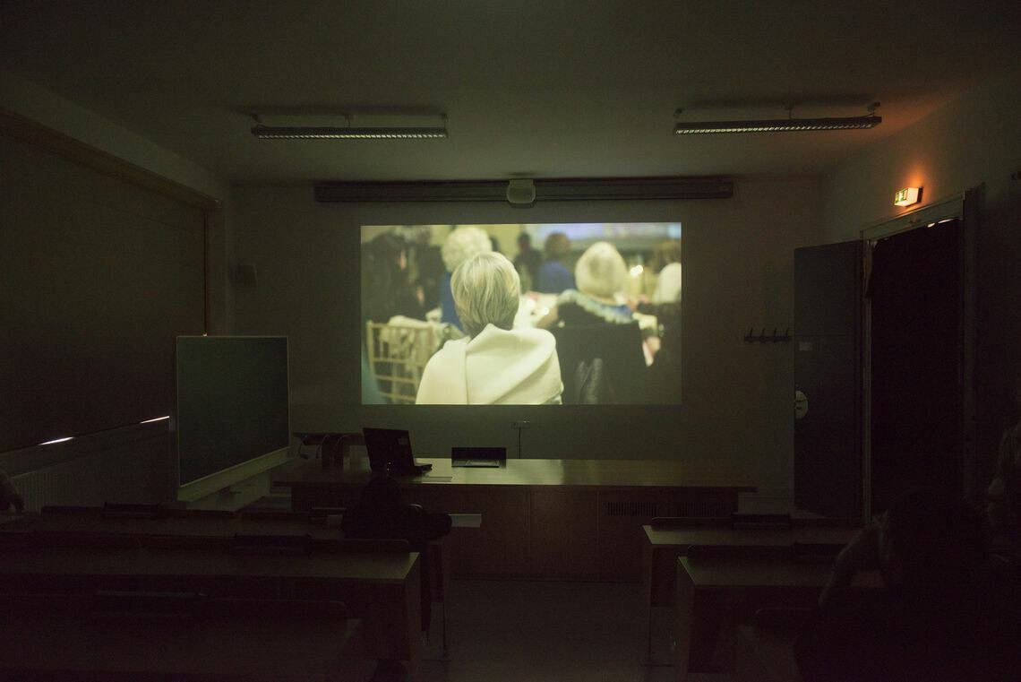 Foto: Ein abgedunkelter Raum in dem Möbel Stegen. An der Wand eine Projektion.