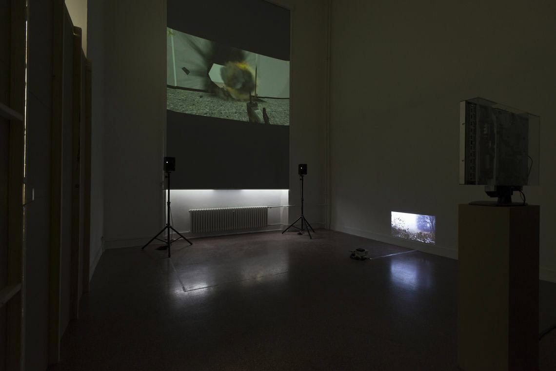 Foto: Ein abgedunkelter Raum. Im Raum befinden sich zwei Lautsprecher auf Stativen und zwei Projektionen, die auf unterschiedlichen Höhen an die Wand geworfen werden.