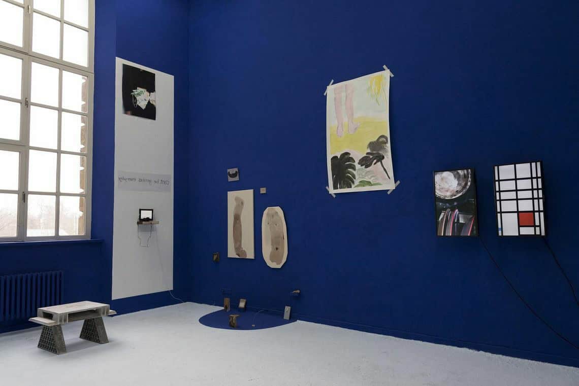 Foto: Ein Raum mit blauer Wand, weißem Boden und großem Fenster. An der Wand hängen, auf unterschiedlichen Höhen, Objekte. Auf dem Boden nahe der Wand ist ein Halbkreis im gleichen Blau wie der Wand aufgemalt. Auf dem Boden des Raumes stehen kleine Objekte und Skulpturen.