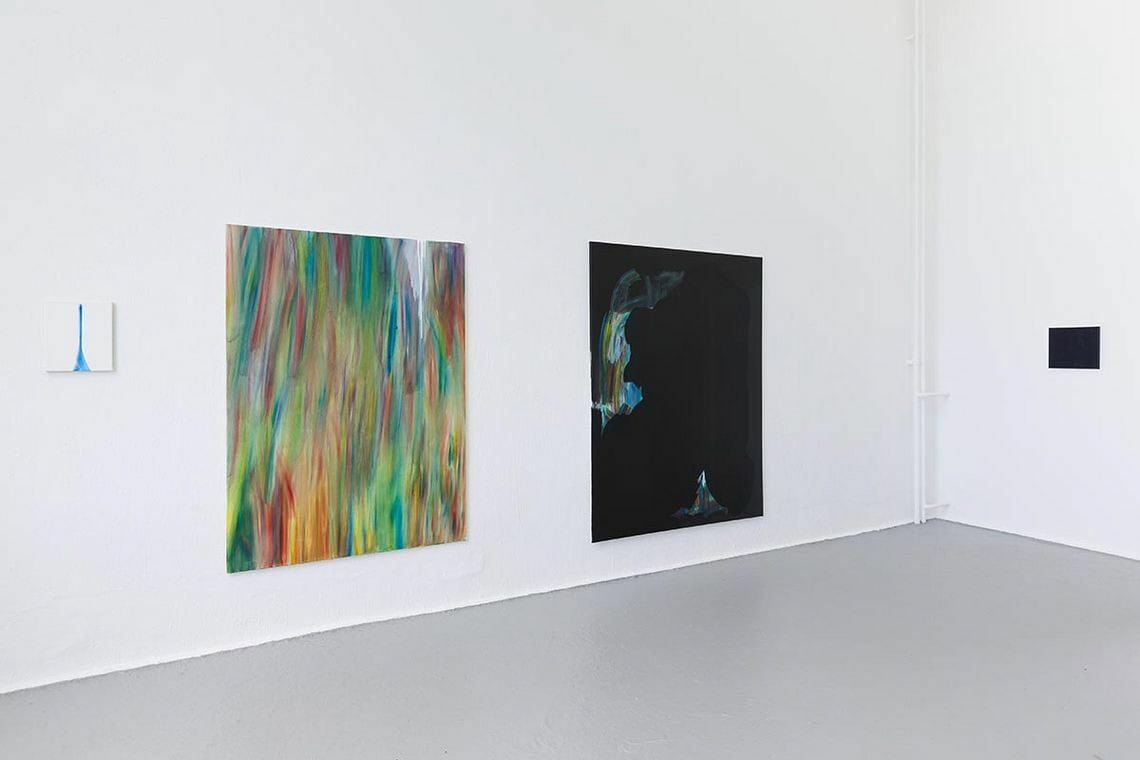 Foto: Ein Raum mit weißen Wänden und grauem Boden. An der Wand hängen Leinwandarbeiten im Klein- und Großformat.