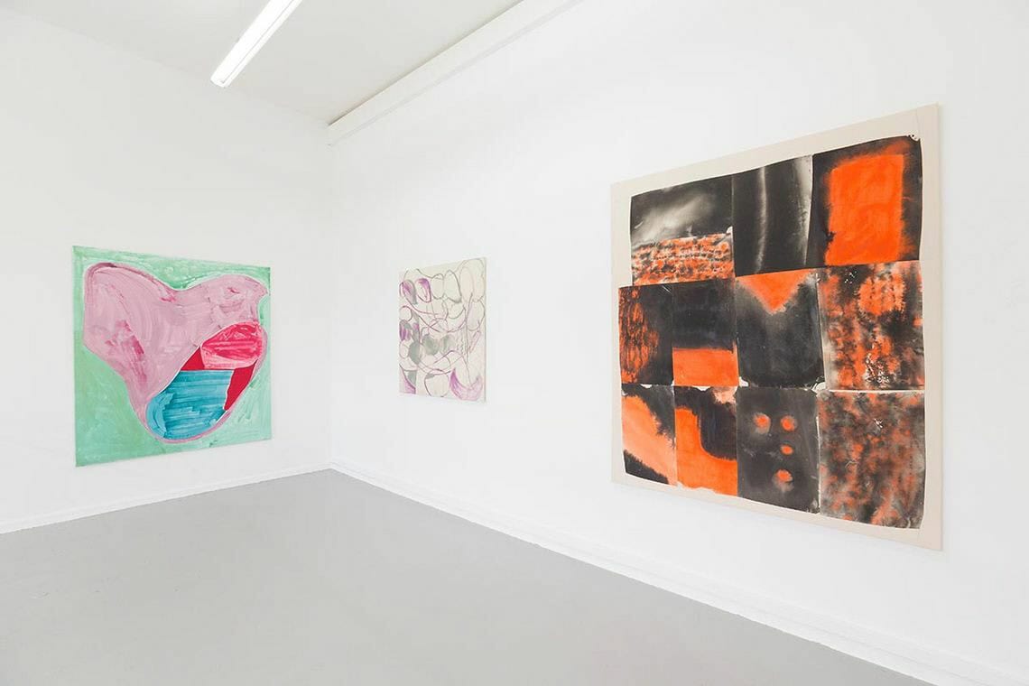 Foto:Ein Raum mit weißen Wänden und grauem Boden. An Den Wänden hängen Leinwände im Mittel- und Großformat.