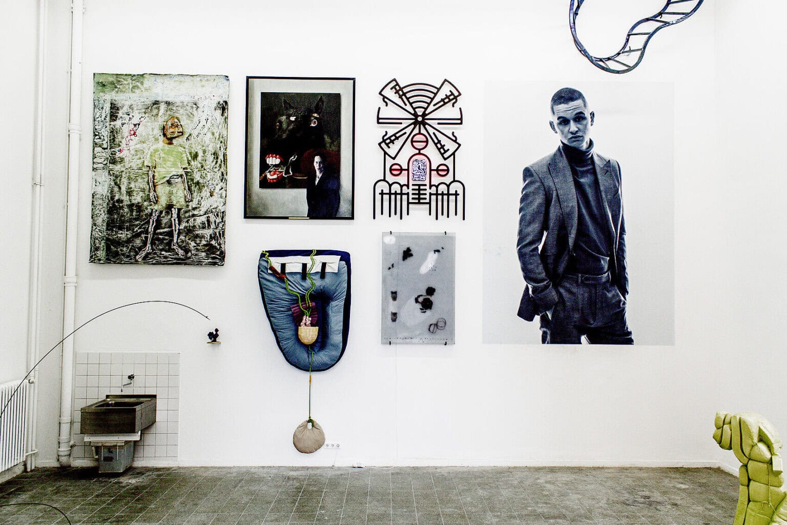 Foto: Ein Raum mit weißen Wänden und grauem, gefliesten Boden. Im Raum stehen zwei Objekte. An der Wand sind neben- und übereinander mehrere großformatige Objekte installiert.