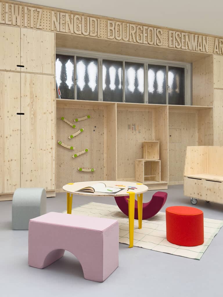 Foto: bunte Schemel um einen niedrigen Tisch, davor eine holzvertäfelte Wand mit Schriftzügen