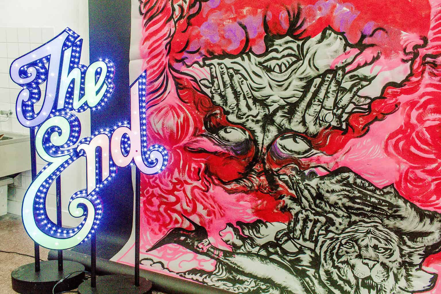 Foto: Nahaufnahme eines Leichtenden Objektes mit dem Schriftzug "The End" vor einer mit färbe bearbeiteten, bunten Fläche.