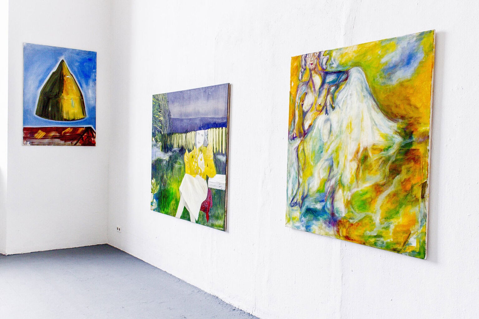 Foto: Raumecke mit weißen Wänden und grauem Boden. An der Wand befinden sich drei Leinwandarbeiten im Mittelformat auf unterschiedlicher Höhe.